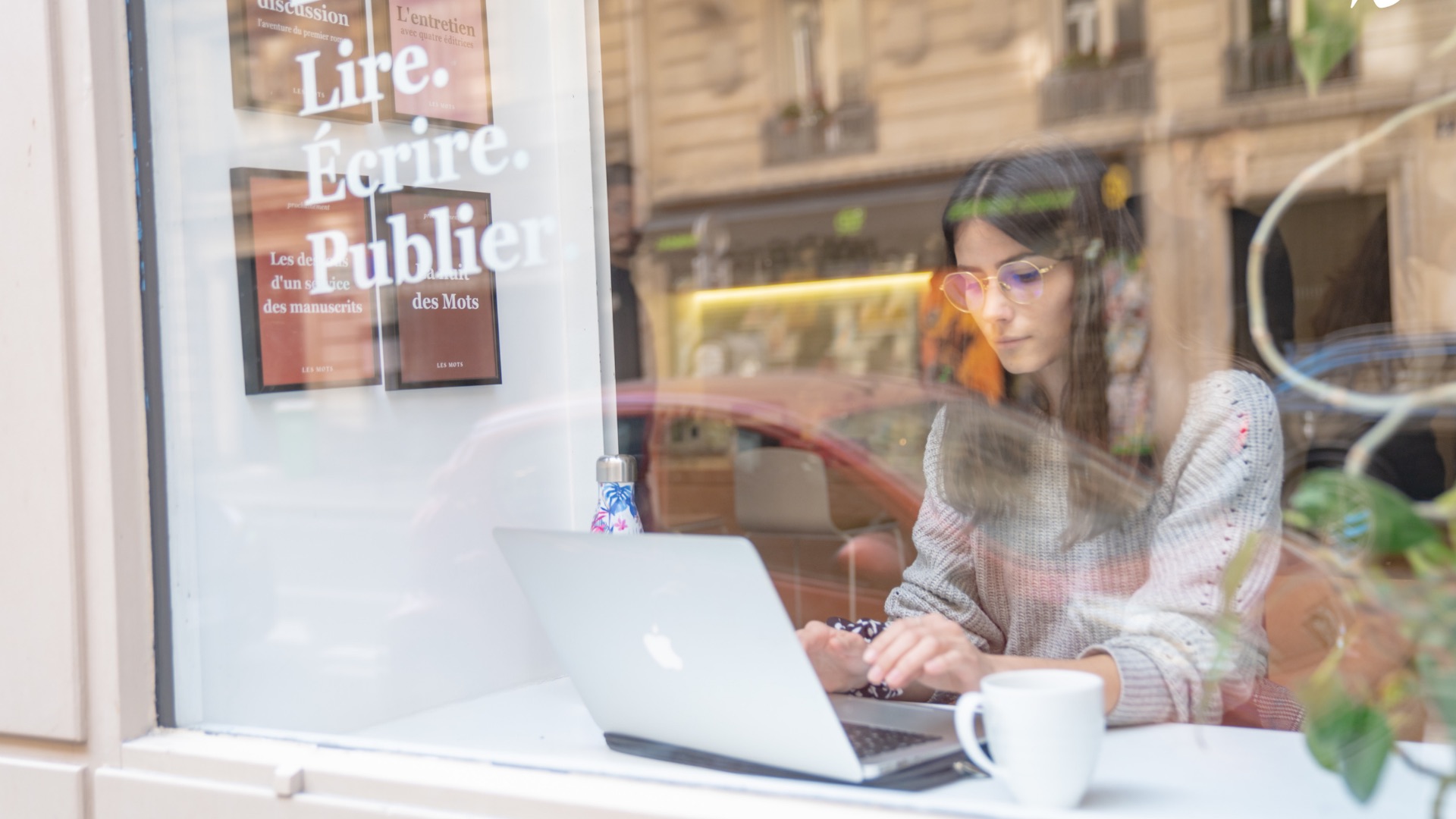 Une élève des Mots travaille sur son ordinateur, derrière la vitrine « Lire. Écrire. Publier »